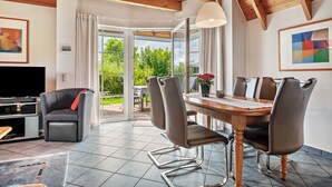 Un salon moderne comprenant un coin repas, des poutres apparentes en bois au plafond, un téléviseur et des œuvres d’art.