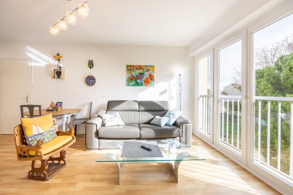 A spacious living room with a grey sofa, a glass coffee table, and a wooden rocking chair.