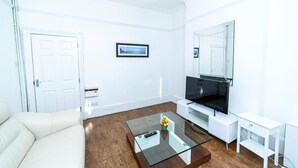 A modern living room with a white sofa, a glass coffee table, a flat-screen TV, and a large mirror.
