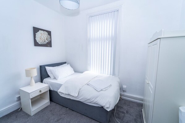A bedroom with a bed, bedside table, lamp, and a wardrobe.