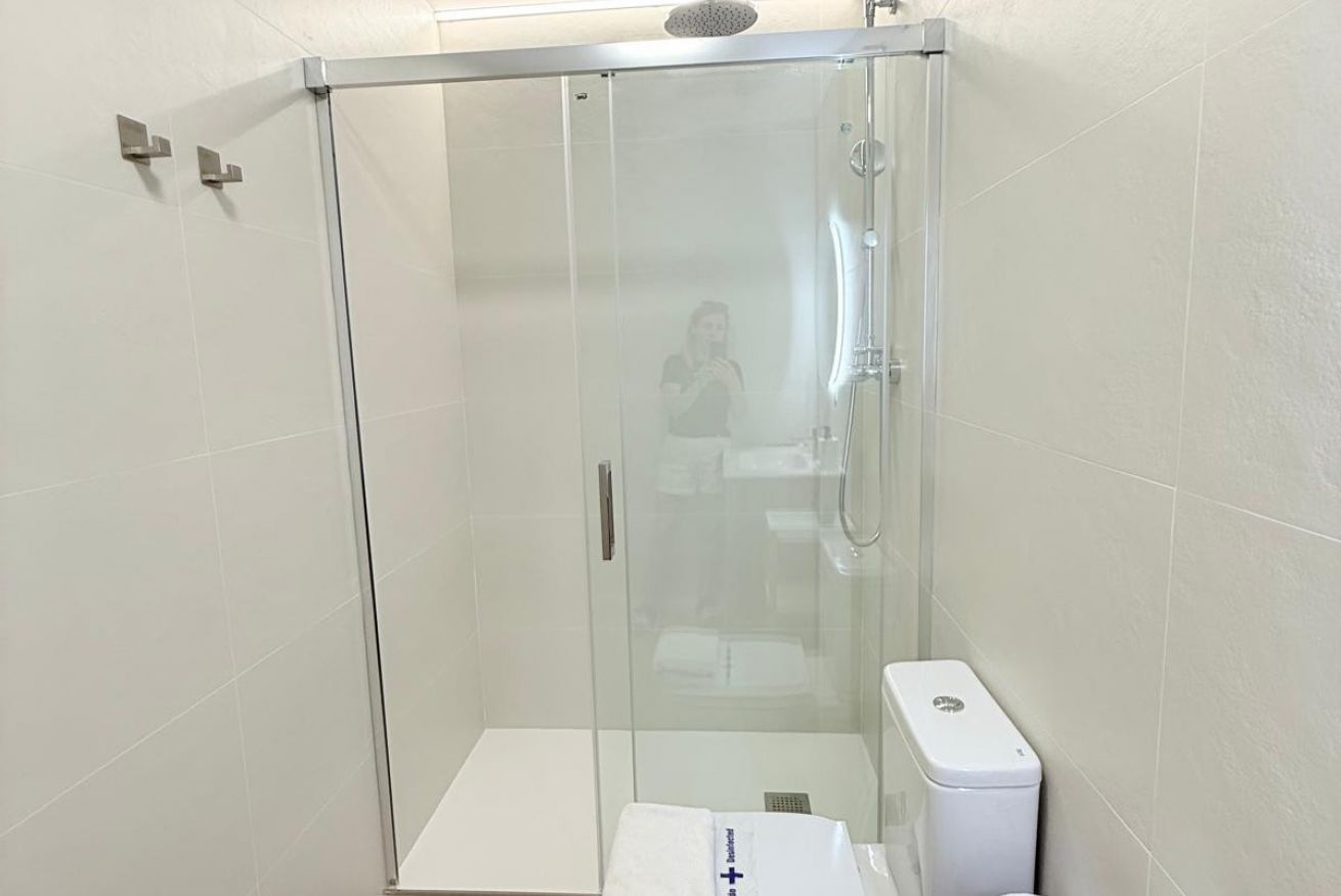 En brusekabine med glasvægge, et hvidt toilet og et håndklæde på gulvet.