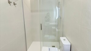 Une cabine de douche fermée par des parois en verre, avec des toilettes blanches et une serviette sur le sol.