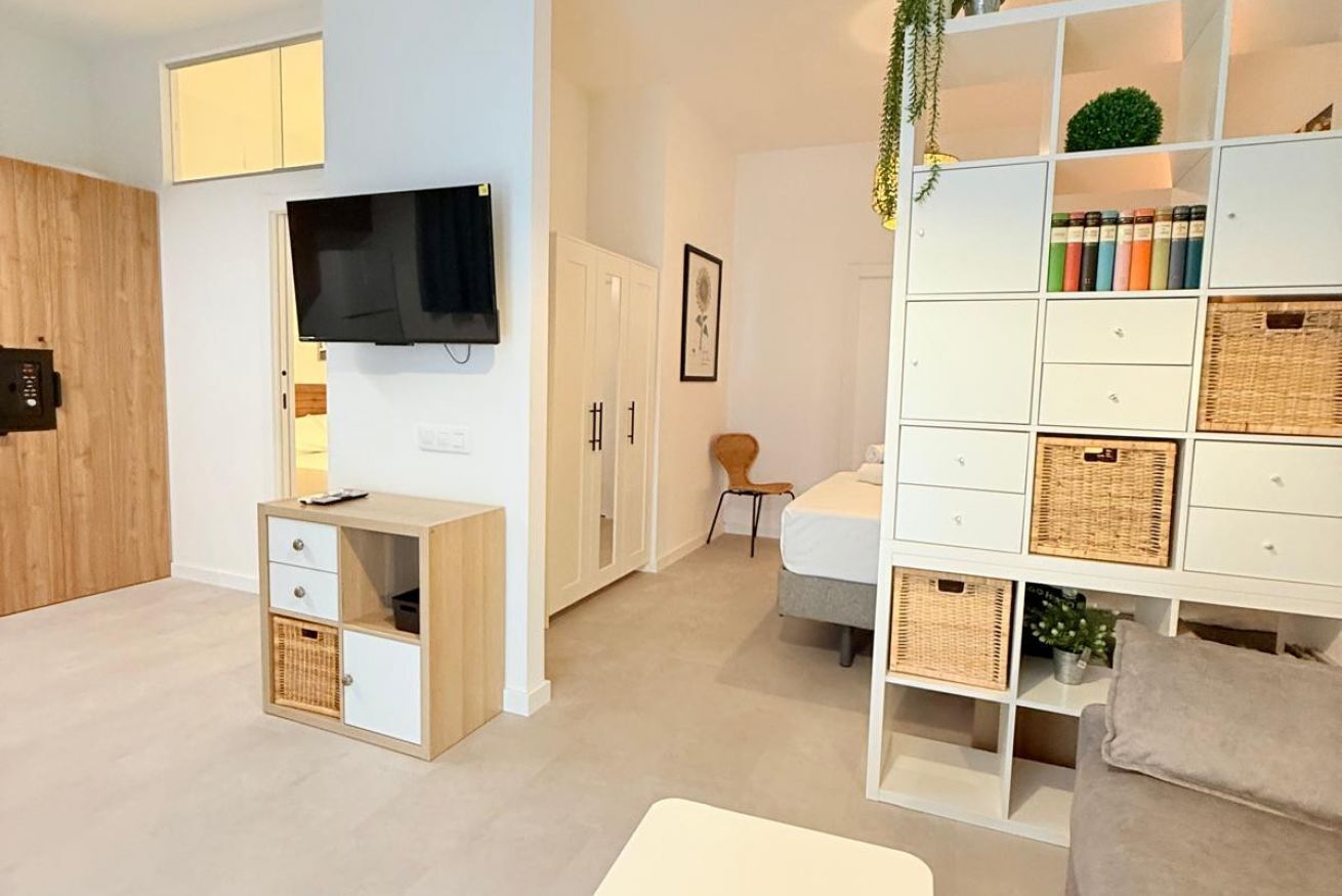 A modern living room with a flat-screen TV, a wooden cabinet, a white sofa, and a bookshelf with wicker baskets.