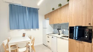 Une cuisine compacte avec un plan de travail blanc, un micro-ondes noir, un lave-vaisselle blanc et des placards en bois.
