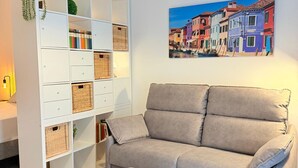 Un salon avec un canapé beige, une table d’appoint blanche et une étagère blanche agrémentée de paniers en osier.