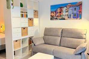 A living room with a beige sofa, a white side table, and a white shelving unit with wicker baskets. -  Oceanografic Suite 1 (València)