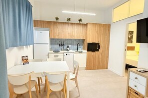 A compact kitchen with a white refrigerator, a coffee machine, and a black microwave. There is a dining table with four chairs and a small cabinet with a television. -  Oceanografic Suite 1 (València)