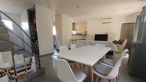 A modern interior with a dining area featuring a white table and chairs, a kitchen in the background, and a staircase leading to another level. - Villa Grape Bubble (L'Isle-sur-la-Sorgue)