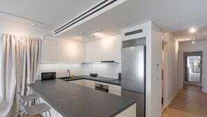 A modern kitchen with a central island, bar stools, a stainless steel refrigerator, and white cabinetry. - LIV Athinum 1 - Luxury Apartment 3A (Athens)