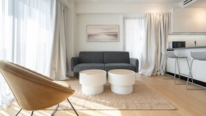 A modern living room with a sofa, two ottomans, a chair, and a kitchen area with a microwave. - LIV Athinum 1 - Luxury Apartment 3A (Athens)