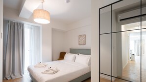 A modern bedroom with a bed, a hanging light, a mirror, and a view of the bathroom. - LIV Athinum 1 - Luxury Apartment 3A (Athens)