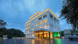 Een modern hotel met een meerlaags gebouw, een overdekte ingang en een groen bord met faciliteiten.
