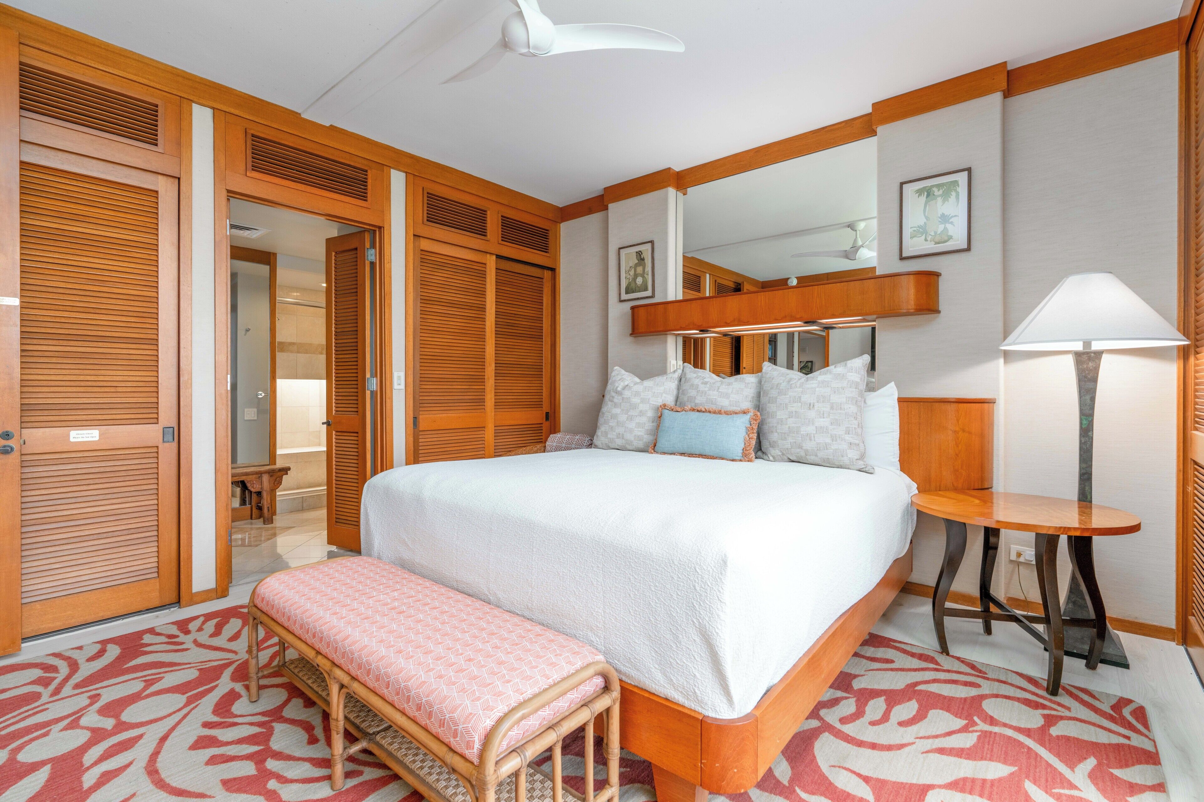 A hotel room with a large bed, a bedside table, a bench, a mirror, and wooden paneling.