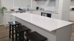 Moderni keittiö, jossa on keskeinen saareke, puiset jakkarat, sisäänrakennettu uuni ja ikkuna tiskialtaan yläpuolella.