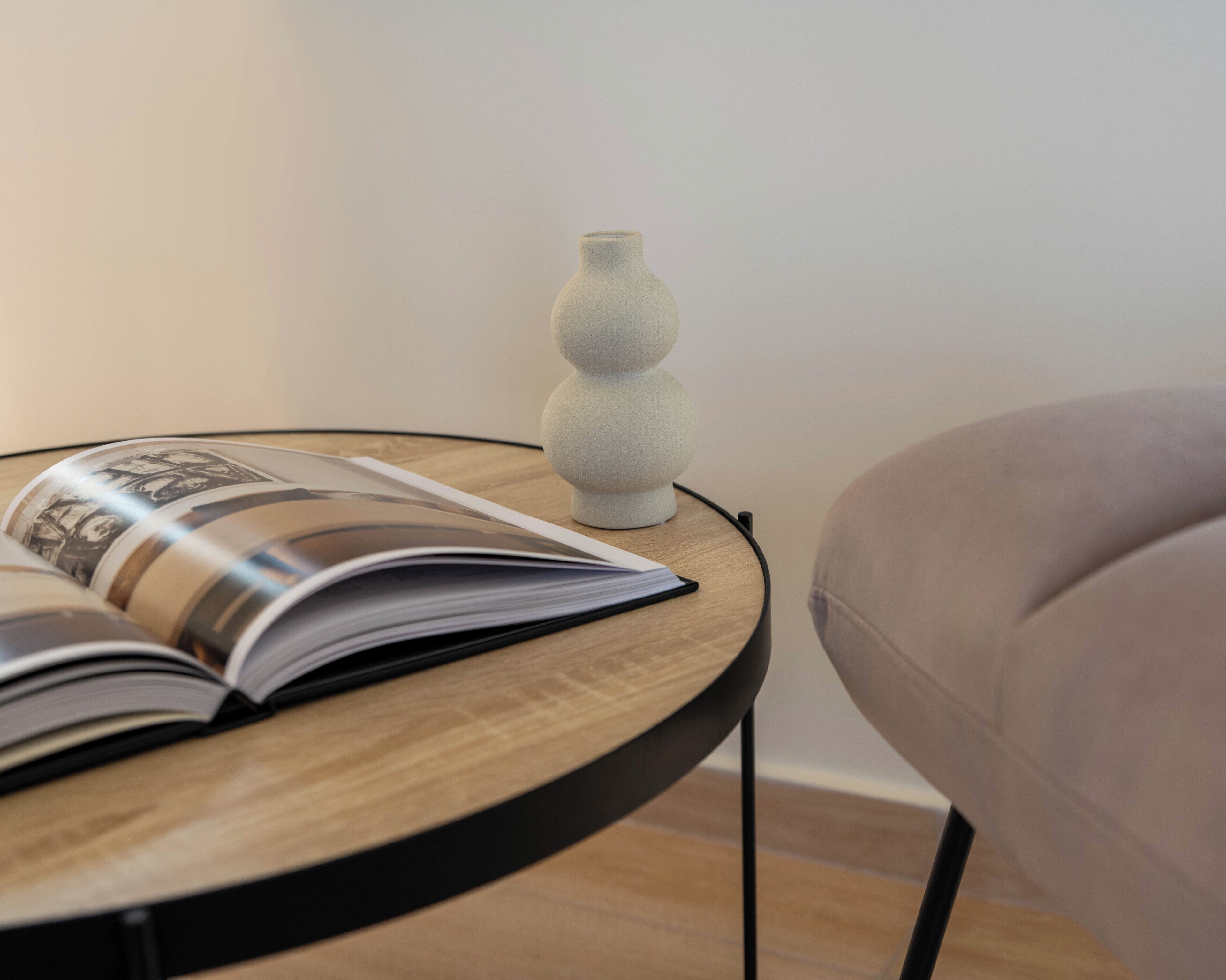 Uma mesinha de madeira redonda com um livro e um vaso branco.