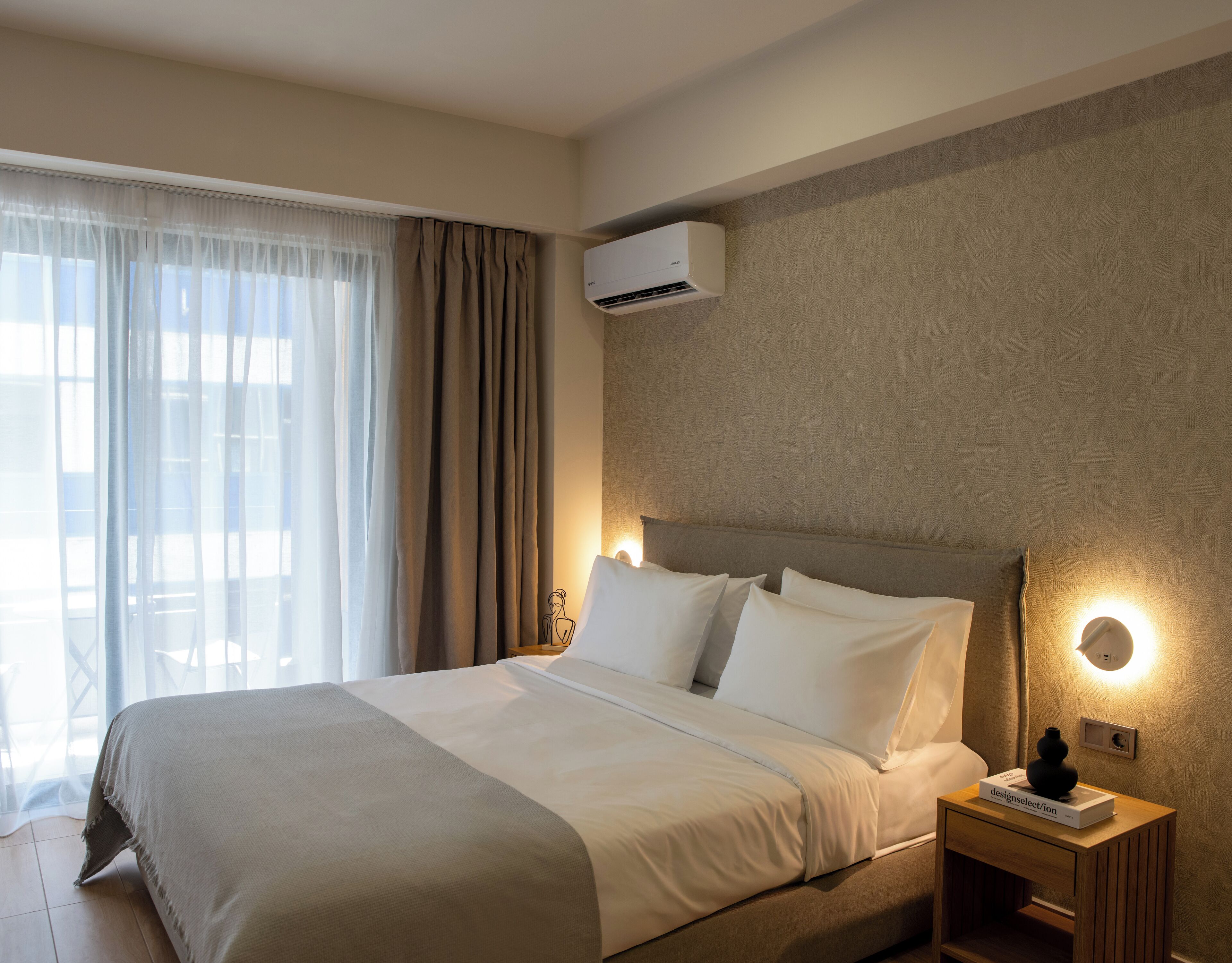 Ein Hotelzimmer mit Bett, Nachttisch mit einem Buch, Klimaanlage und einem fenster mit Vorhängen.