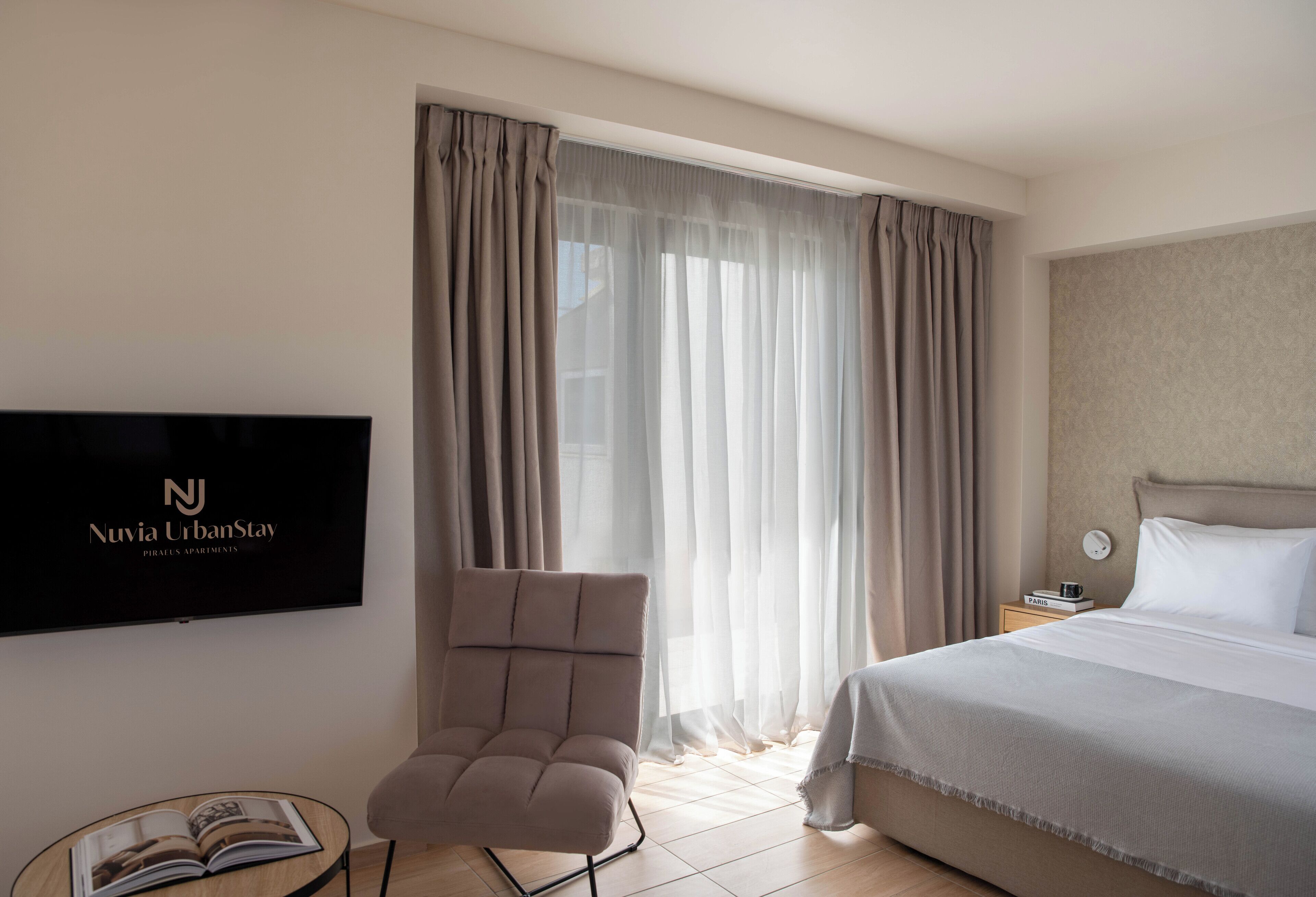 A hotel room with a bed, a chair, a TV, and a window with curtains.