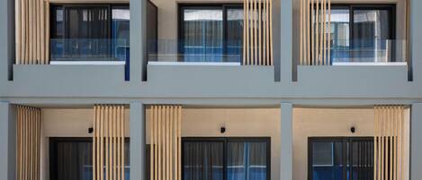 A modern building with a symmetrical facade, featuring multiple balconies with glass railings and vertical wooden slats.