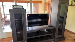 A dark wooden entertainment center with a flat-screen TV, a W-KING speaker, and a shelf.