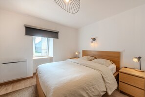 A bedroom with a bed, bedside tables, a window, a radiator, and a ceiling light fixture.