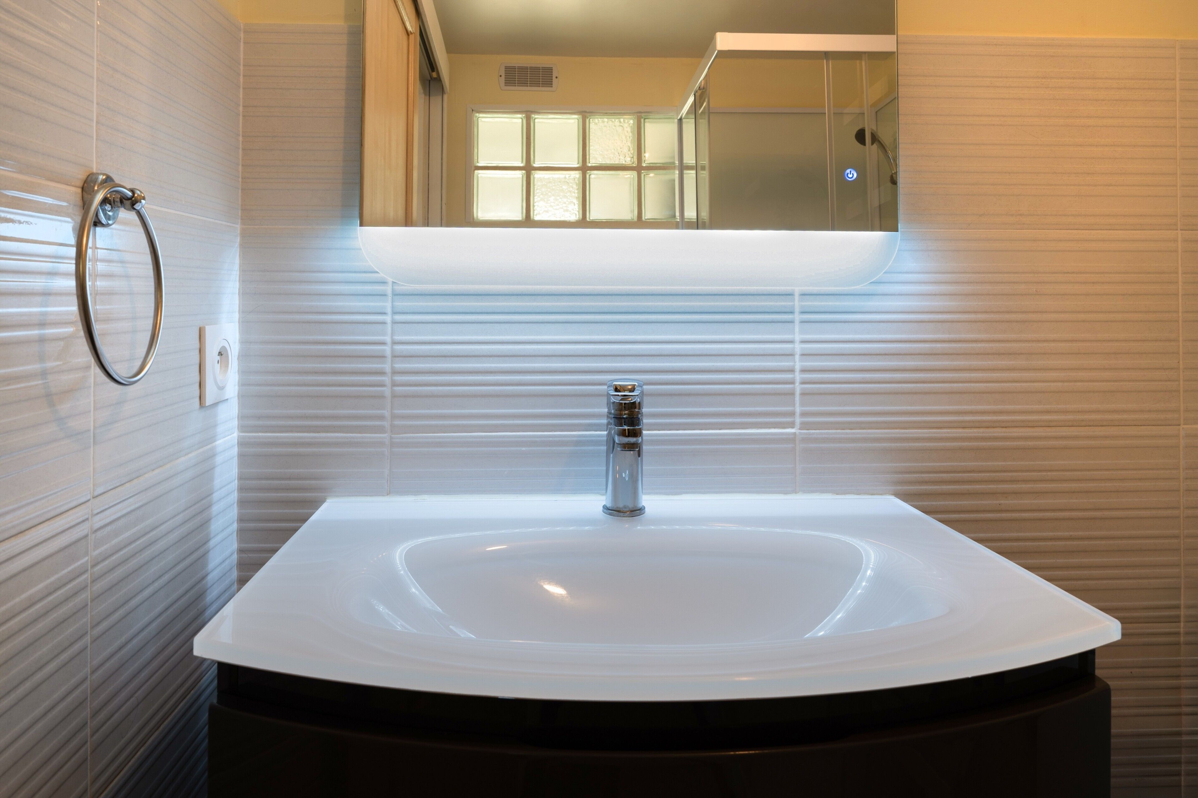 A modern bathroom with a large white sink, a chrome faucet, and a glass-enclosed shower.