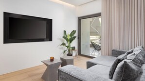 Una sala de estar moderna con un televisor de pantalla plana montado en la pared, un sofá gris, una mesita auxiliar y una planta en maceta.