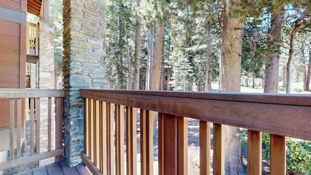 Un balcon doté d’un mur en pierre et d’une balustrade en bois, donnant sur une zone boisée.