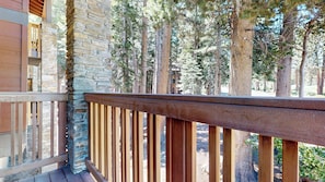 A balcony with a stone wall and wooden railing, overlooking a forested area.