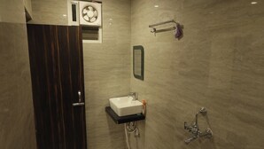 A modern bathroom with a dark wood door, a white sink, a mirror, a towel rack, and a handheld showerhead. - Hotel Kingston (Ranchi)