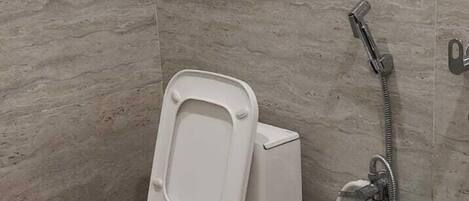 A bathroom with a toilet, a shower, and a large beige bucket.