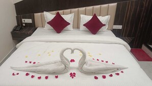 A hotel room with a bed featuring a heart-shaped towel arrangement and rose petals. - Hotel Kingston (Ranchi)