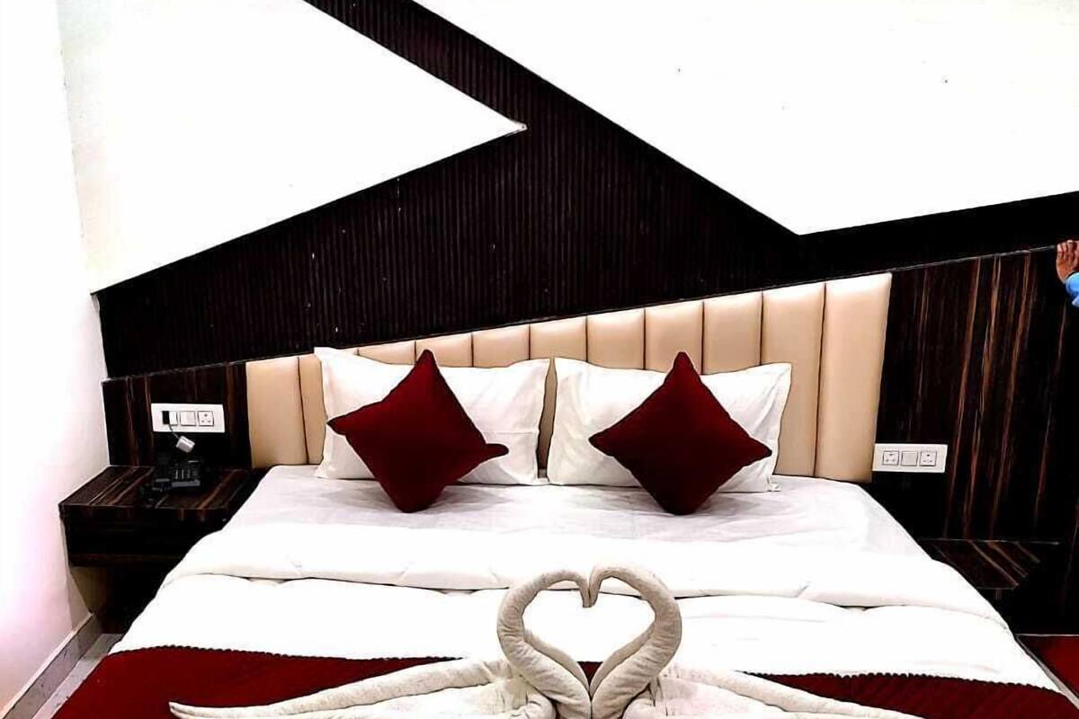 A hotel room with a bed, two red pillows, a heart-shaped towel arrangement, and a modern geometric wall design.
