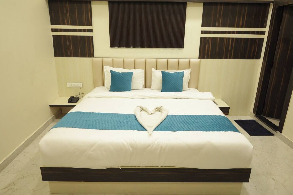 A neatly made bed with a heart-shaped pillow arrangement, a bedside phone, and a nightstand.