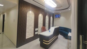 A reception area with a reception desk, a blue sofa, a flat-screen TV mounted on the wall, and a patterned wall design. - Hotel Kingston (Ranchi)
