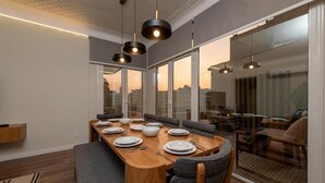 A modern dining area with a wooden table set for four, large windows, and a view of the cityscape. - Kennah Lasciac | 3BR Near Tahrir Sq., Downtown (Cairo)