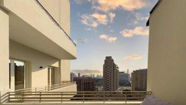 A balcony with a sofa and a tiled floor, overlooking a cityscape with buildings and a clear sky. - Kennah Lasciac | 3BR Near Tahrir Sq., Downtown (Cairo)