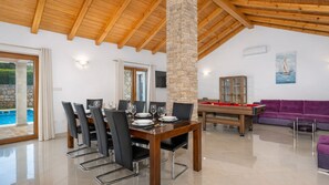 A spacious room with a wooden ceiling, a dining table set for six, a pool table, and a purple sofa.