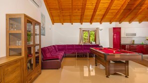 Une pièce comprenant une table de billard, un canapé, un meuble avec des portes en verre et une fenêtre avec des rideaux.