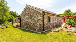 Un bâtiment en pierre avec un toit en tuiles, une cour gazonnée et une balançoire.