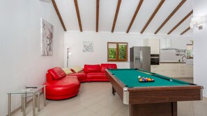 A room with a pool table, red leather sofa, and a kitchen area.