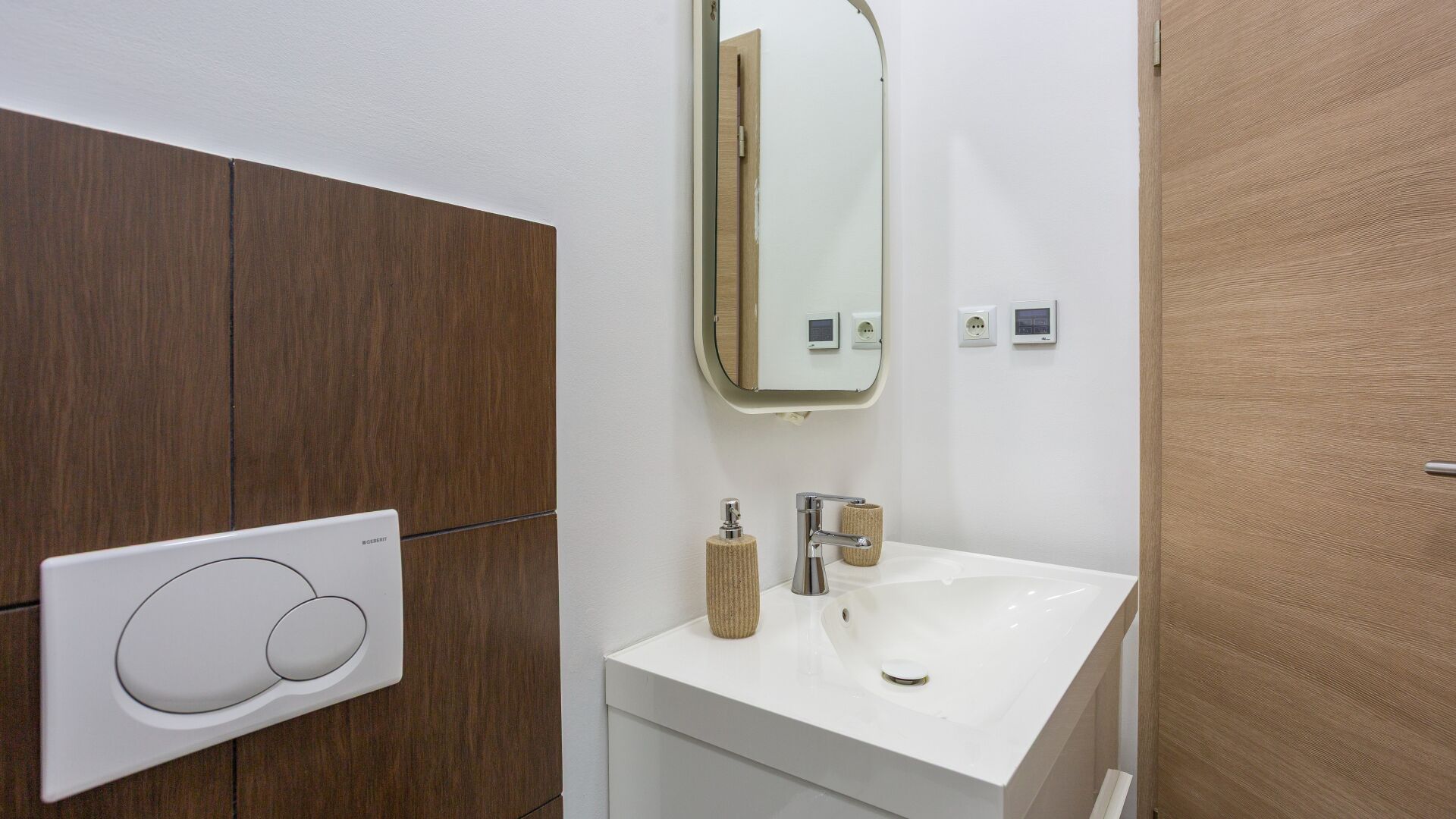 A bathroom with a white sink, a mirror, a towel dispenser, and a wall-mounted control panel.