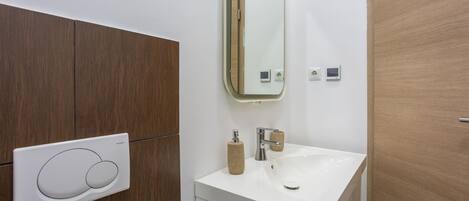 A bathroom with a white sink, a mirror, a towel dispenser, and a wall-mounted control panel.