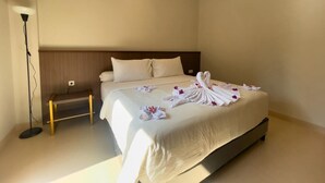 Un lit bien fait, avec du linge de lit blanc et un arrangement floral, une table de chevet et une lampe sur pied dans une chambre d’hôtel.