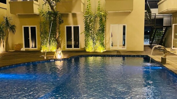 Une piscine offrant une vue sur un immeuble à plusieurs étages, doté de balcons et de fenêtres.