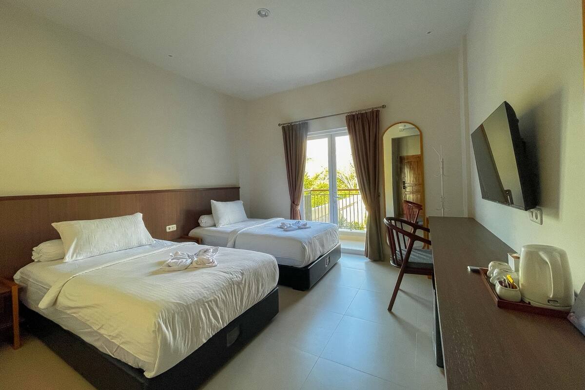 A hotel room with two beds, a desk, a chair, a TV, and a balcony with curtains.