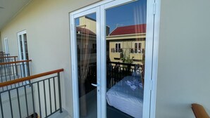 Un balcon doté d’une porte-fenêtre coulissante, d’une rambarde en bois et d’un lit avec un matelas blanc et un oreiller bleu.