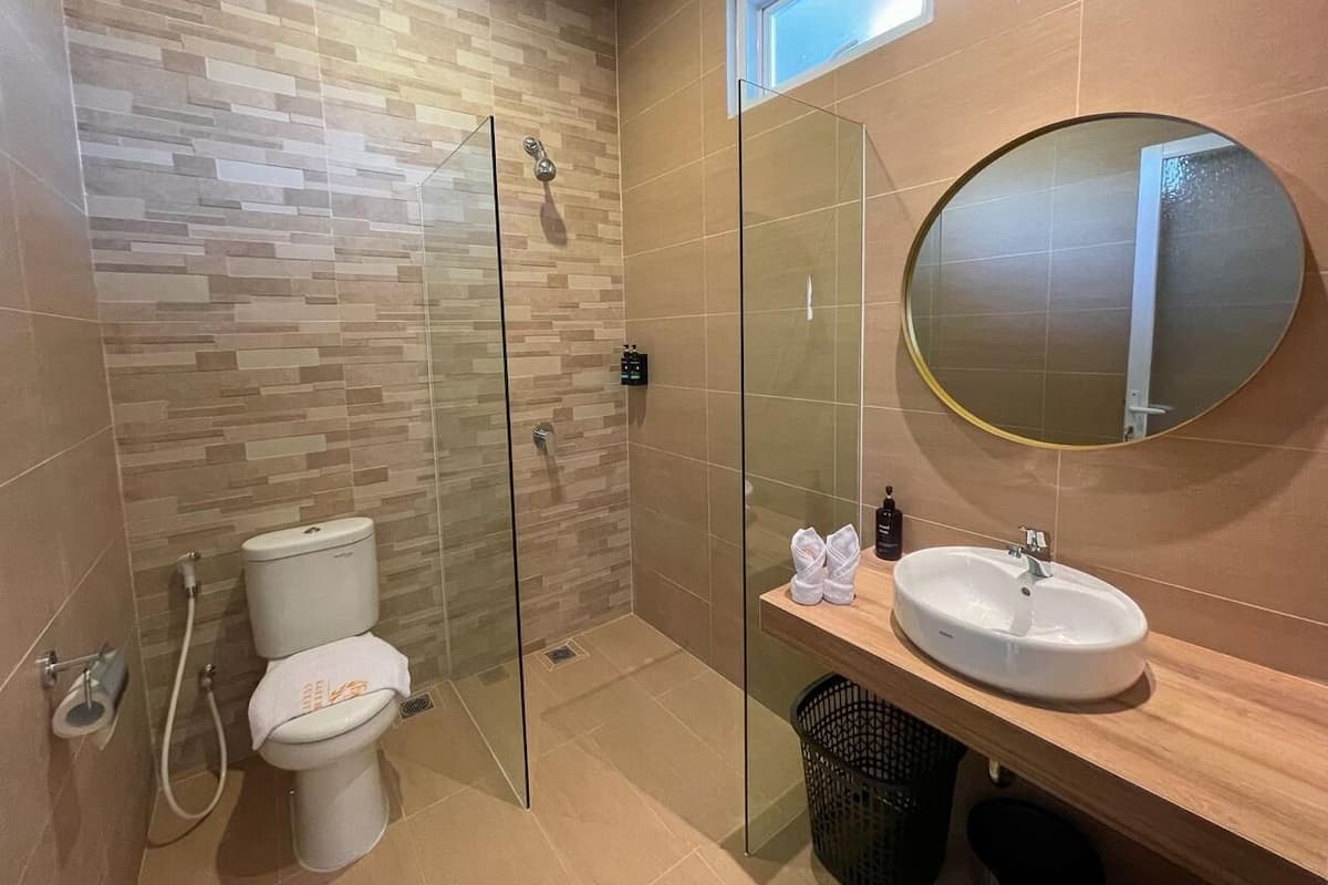 A modern bathroom with a glass-enclosed shower, a toilet, a sink with a mirror, and a window above the sink.