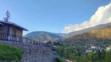 A stone wall, a building with a balcony, and a mountainous landscape with houses.