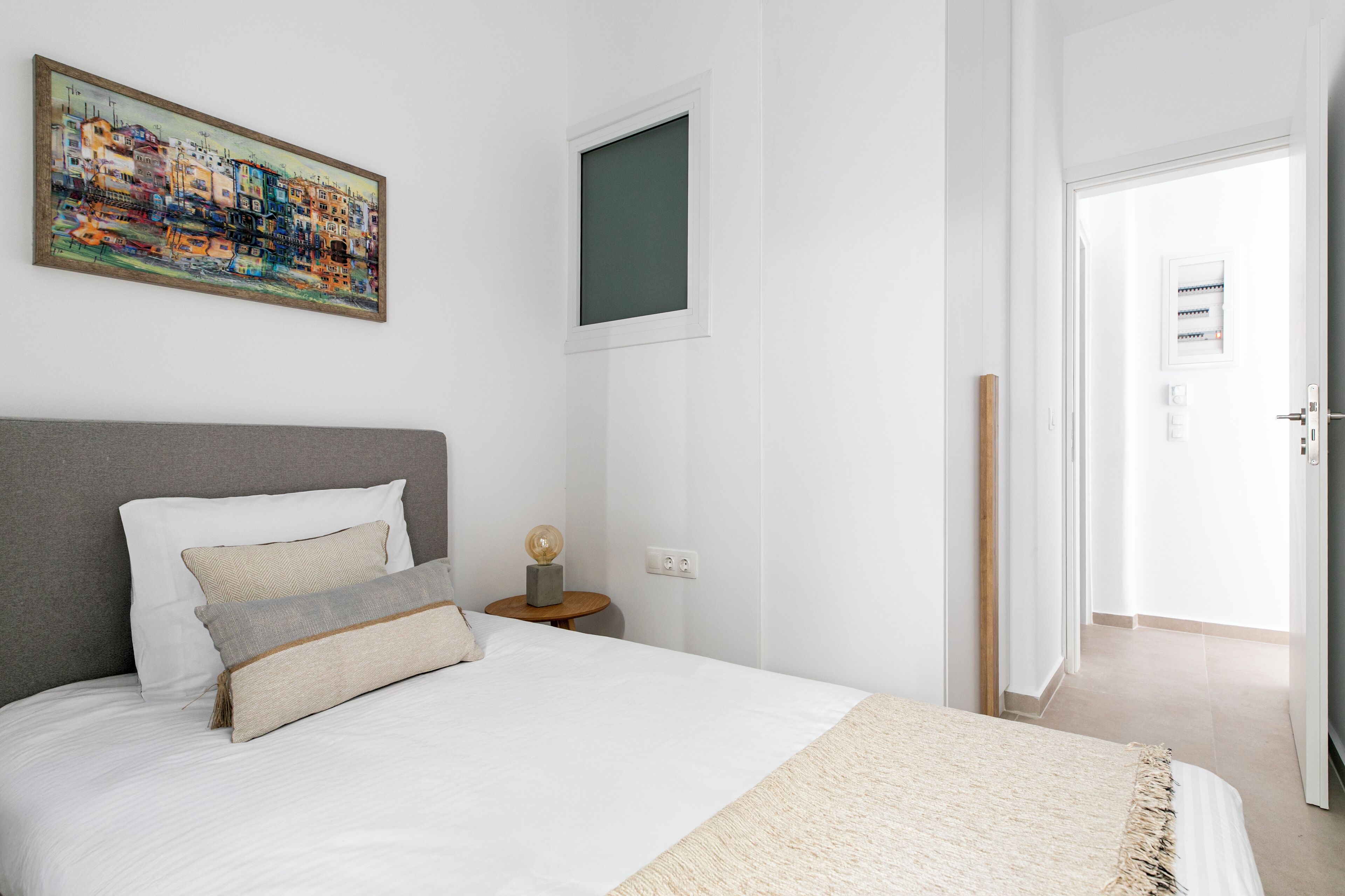 Un dormitorio con una cama grande, una mesita de noche, un cuadro y una ventana.