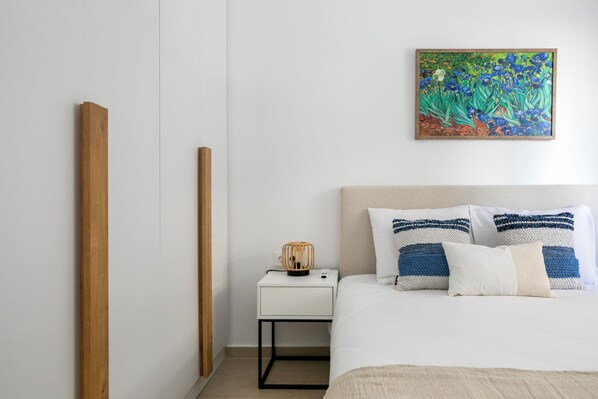 Een keurig opgemaakt slaapkamer met een bed, nachtkastje en een schilderij aan de muur.
